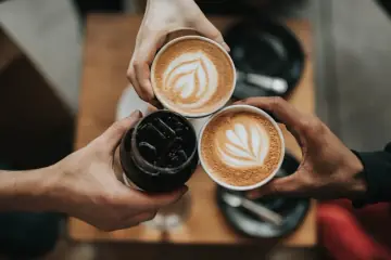 Drei Kaffeetassen, von Freunden um einen Tisch gehalten